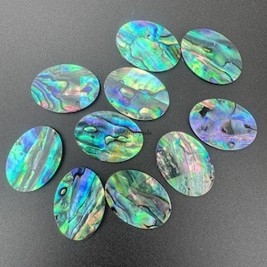 May include: Ten oval-shaped abalone shell pieces with iridescent green, blue, and purple colors. The shells have a natural, organic texture.