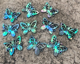 May include: A collection of iridescent butterfly-shaped pendants. The pendants feature a mix of blue, green, and purple hues, with intricate cut-out designs. The butterflies are arranged on a textured, gray surface, showcasing their decorative appeal.
