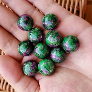 Könnte beinhalten: Eine Sammlung von zehn grünen und violetten Edelsteinkugeln. Die Kugeln sind glatt und poliert und weisen eine Vielzahl von Mustern und Wirbeln auf.