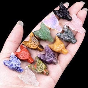 May include: A collection of 12 wolf head carvings made from various gemstones, including amethyst, tiger's eye, clear quartz, and rose quartz.