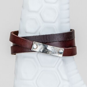 May include: A brown leather wrap bracelet with a silver metal plate and two silver rivets.