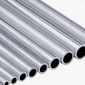 May include: A collection of silver-colored metal tubes of varying diameters, arranged diagonally. The tubes have a smooth, reflective surface and a hollow interior, with the open ends appearing black. The tubes are likely used for construction or industrial purposes.