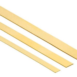 May include: Three flat, golden-yellow strips of wood, varying in width, are arranged diagonally against a white background. The strips appear to be new and unused, with a smooth, clean surface. The wood has a natural, warm tone.