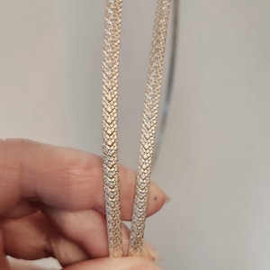 May include: Two silver-colored, textured headbands. The headbands have a repeating pattern of small, raised shapes. The headbands are held in a person's hand against a neutral background. The headbands are thin and flexible.