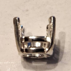 May include: A shiny, silver-colored metal charm in the shape of the 'rock on' hand gesture. The charm has a detailed design with a smooth, reflective surface. The charm is likely for jewelry or a similar craft.