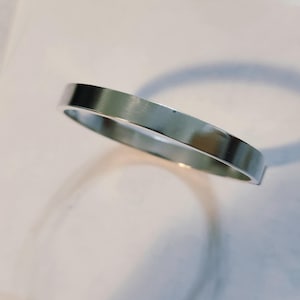 May include: A simple, polished silver-tone metal band ring with a flat, smooth outer surface and a circular shape. The ring has a reflective finish that catches the light, creating a clean, uniform appearance without any engravings or stones.