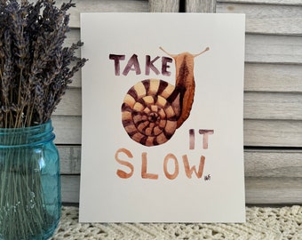 May include: A watercolor illustration of a snail with the text "TAKE IT SLOW" in brown and pink lettering. The snail is brown and has a striped shell.