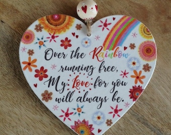 May include: A heart-shaped wooden decoration featuring a rainbow and floral pattern. The text reads "Over the Rainbow, running free, My love for you will always be." A string and wooden bead are attached for hanging.