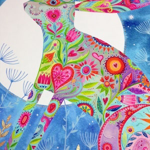 Op de afbeelding: Een kleurrijke, gedetailleerde illustratie van een konijn dat gesilhouetteerd is tegen een blauwe maan. Het konijn is bedekt met een patroon van bloemen, harten en paisley-ontwerpen in tinten roze, paars, groen en geel. De achtergrond is een lichtblauwe aquarelwas met witte sterren.