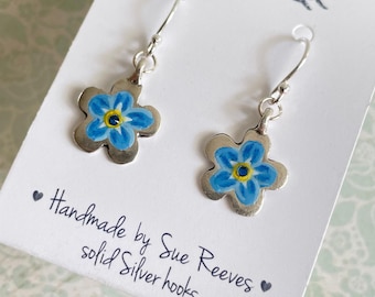 Może przedstawiać: Srebrne kolczyki z niebiesko-żółtymi motywami kwiatowymi. Kolczyki są na białej karcie z napisem "Handmade by Sue Reeves solid Silver hooks" i ilustracją królika.
