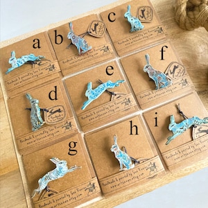 Könnte beinhalten: Eine Sammlung von neun hasenförmigen Ornamenten, die jeweils mit einem Buchstaben von a bis i gekennzeichnet sind. Die Ornamente sind in Blau- und Weißtönen mit komplizierten Blumenmustern bemalt und auf braunen Pappkarten befestigt.