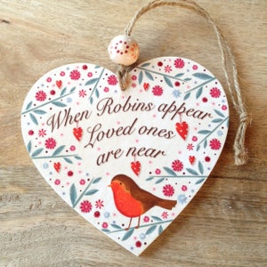 May include: Heart-shaped wooden plaque with the text "When Robins appear Loved ones are near." The plaque features a robin, red hearts, and floral accents in pink, red, and blue. A jute string and a decorative bead are attached for hanging.