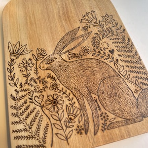 Ein Schneidebrett mit einem detaillierten sitzenden Hasen und Blumen, die mittels Brandmalerei in das Holz gebrannt wurden. Auf der Rückseite glatt. Hase Liebhaber Geschenk
