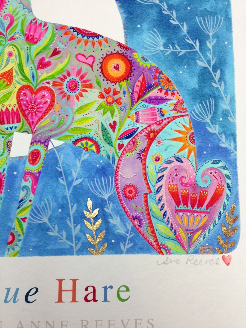 Op de afbeelding: Een kleurrijk aquarel schilderij van een blauwe haas met een bloemenpatroon. De haas is omringd door een blauwe achtergrond met gouden accenten. Het schilderij is onderaan rechts gesigneerd met "Jane Reeves" en onderaan links met "Blue Hare" betiteld.