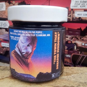 May include: A black glass jar with a white lid. The jar has a label with a graphic of a man wearing a white mask and the text "The Town That Dreaded Sundown". The text "In 1946 this man killed five people... Today he still lurks the streets of Texarkana, Ark." is also on the label.