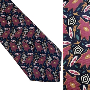 May include: A patterned necktie featuring a repeating geometric design in navy blue, burgundy, gold, and white. The tie has a diagonal orientation, showcasing the intricate pattern of the fabric. The design includes pentagon shapes and oval accents.