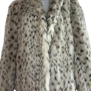 May include: A long-sleeved faux fur jacket featuring a white base color with a dense pattern of dark brown and black spots. The jacket has a high collar, a straight front opening, and a thick, textured pile that covers the entire exterior surface.
