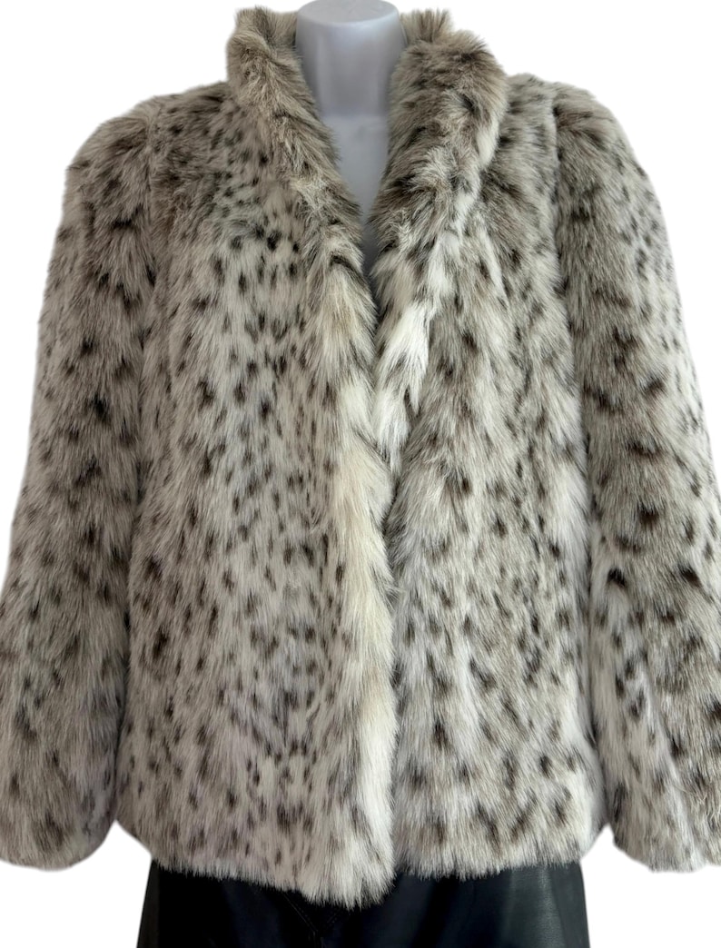May include: A long-sleeved faux fur jacket featuring a white base color with a dense pattern of dark brown and black spots. The jacket has a high collar, a straight front opening, and a thick, textured pile that covers the entire exterior surface.