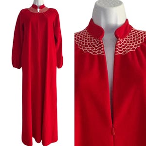 May include: A floor-length red robe featuring long sleeves with elasticized cuffs, a mandarin collar, and a front zipper closure. The neckline is accented with a white lattice-style embroidered pattern that extends across the upper chest area.