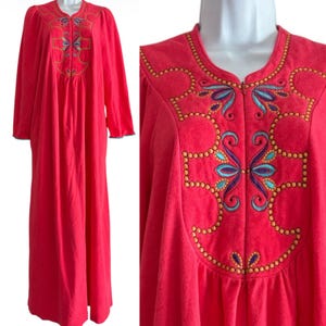 May include: A floor-length, bright red robe featuring long sleeves and a front zipper closure. The chest area is decorated with intricate embroidery in shades of gold, teal, and purple, arranged in a symmetrical, scrolling pattern.