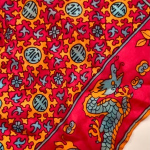 May include: A vibrant red silk scarf with an intricate pattern of orange and teal shapes and symbols. The border features a teal and orange dragon design. This scarf is a stylish accessory.