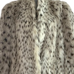 May include: A long-sleeved coat featuring a thick, textured faux fur material with a cream-colored base and a repeating pattern of dark brown and black spots throughout the entire garment, including a high collar and a straight front opening.