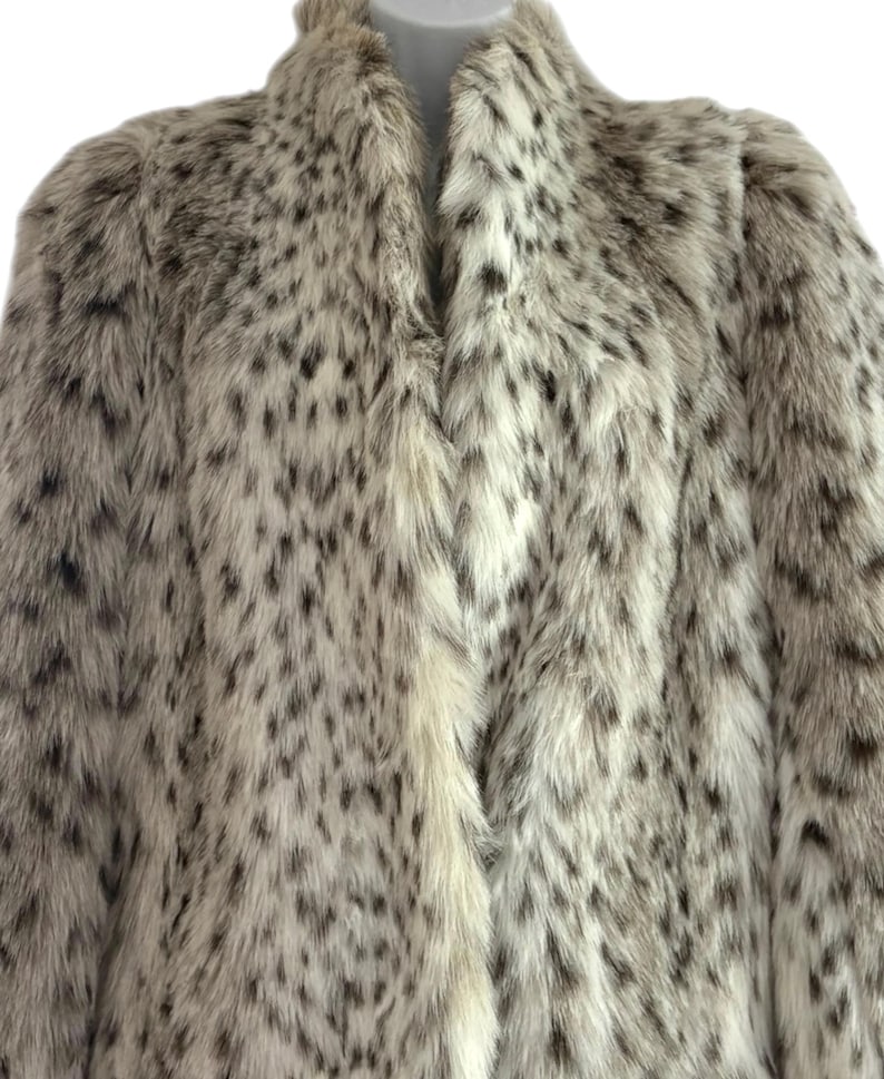 May include: A long-sleeved coat featuring a thick, textured faux fur material with a cream-colored base and a repeating pattern of dark brown and black spots throughout the entire garment, including a high collar and a straight front opening.