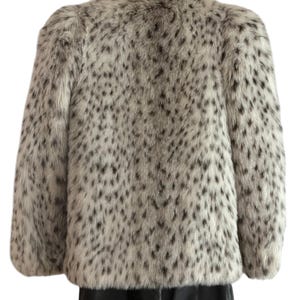 May include: A long-sleeved jacket featuring a faux fur texture with a white base color and a dense pattern of small, irregular black spots throughout. The garment has a structured shoulder design and a straight hemline, providing a consistent look.