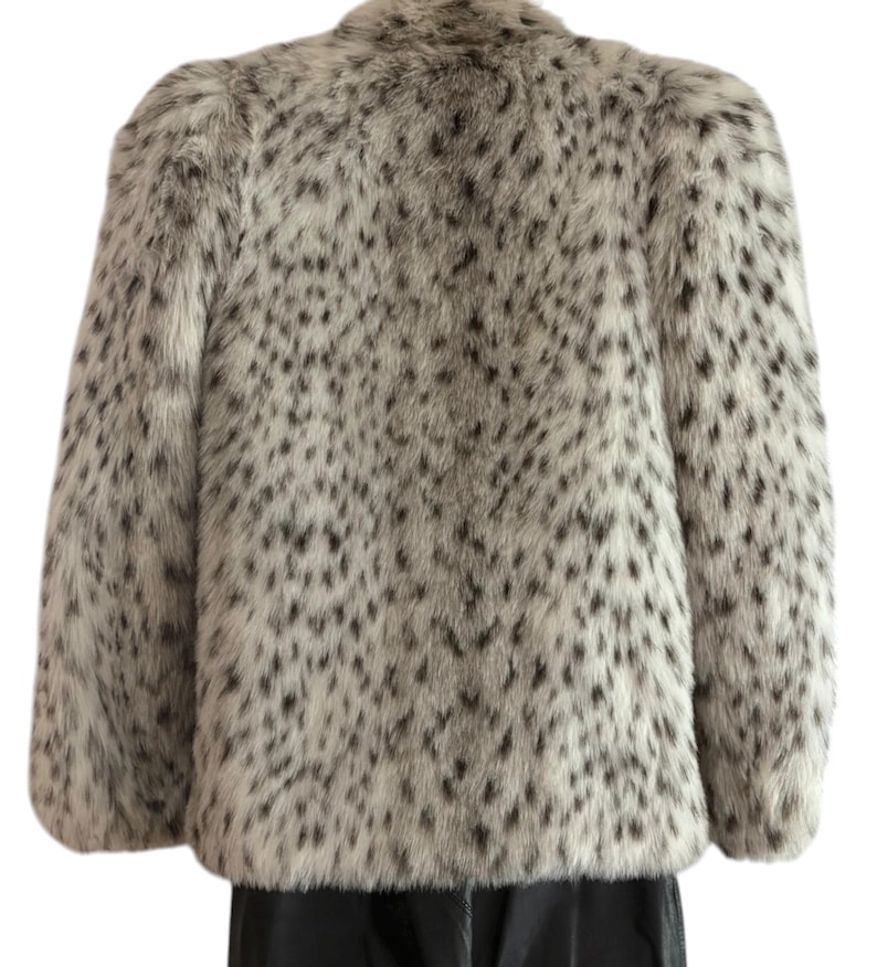 May include: A long-sleeved jacket featuring a faux fur texture with a white base color and a dense pattern of small, irregular black spots throughout. The garment has a structured shoulder design and a straight hemline, providing a consistent look.