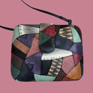May include: A patchwork crossbody bag with a rectangular shape and a flap closure. The bag features a variety of textures and colors, including green, black, brown, and purple. It has a long, thin strap.