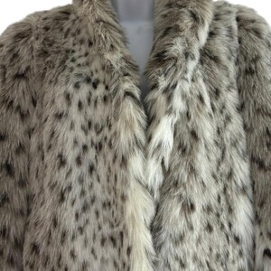 May include: A long-sleeved coat made of faux fur with a thick, plush collar. The garment features a light cream and beige base color with a dense pattern of dark brown and black spots distributed across the entire surface of the textured material.