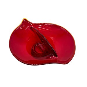 May include: A vibrant red glass bowl with a unique, organic shape. The bowl has a glossy finish and a thin, golden-yellow rim. The design features a central indentation and a curved, asymmetrical form, perfect for decorative use.