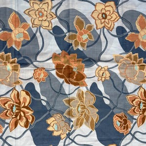 May include: A fabric featuring a repeating pattern of stylized brown and tan flowers with small light blue centers. The floral design is set against a background of dark blue and light gray organic shapes connected by thin, dark blue wavy lines.