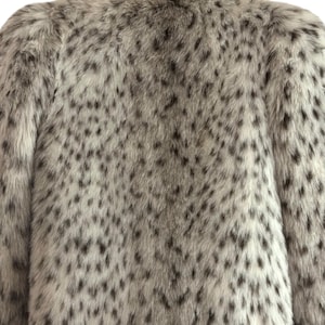 May include: A long-sleeved coat featuring a dense, plush faux fur texture. The garment displays a light gray and white base color with a repeating pattern of dark gray to black irregular spots distributed across the entire surface of the fabric.