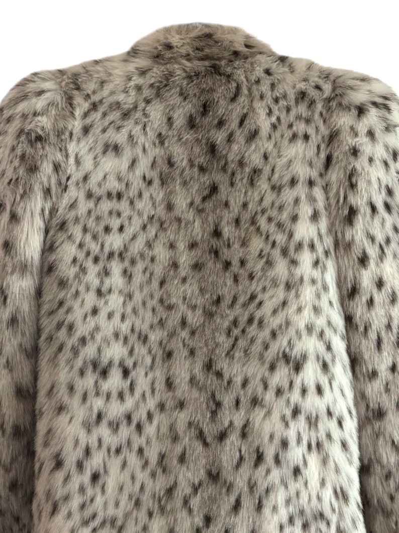 May include: A long-sleeved coat featuring a dense, plush faux fur texture. The garment displays a light gray and white base color with a repeating pattern of dark gray to black irregular spots distributed across the entire surface of the fabric.