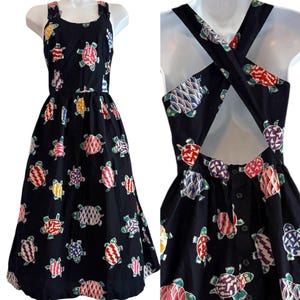 May include: A black midi dress featuring a repeating pattern of colorful turtles in shades of red, yellow, purple, and blue. The dress has a scoop neckline, wide shoulder straps, and a back design with crisscross straps and a button-down closure.