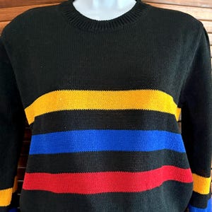 Pu&ograve; includere: Maglione nero con strisce orizzontali gialle, blu e rosse. Il maglione ha un girocollo e polsini e orlo a coste. Le strisce sono uniformemente distanziate sul petto e sulle maniche.