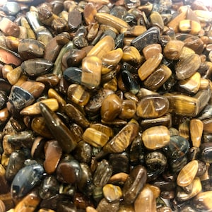 May include: A collection of polished tiger's eye stones, displaying a range of sizes and shapes. The stones exhibit a blend of brown, gold, and black hues. The surfaces are smooth and reflective, presenting a natural, earthy aesthetic.