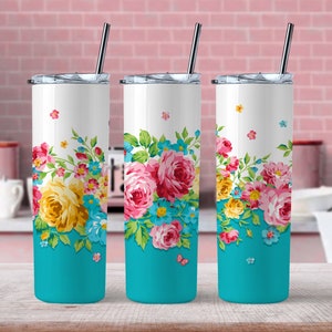 May include: Three white insulated tumblers with floral designs. Each tumbler has a turquoise base, a white upper section, and a colourful floral pattern of pink, yellow, and blue flowers. The tumblers have silver lids and straws.