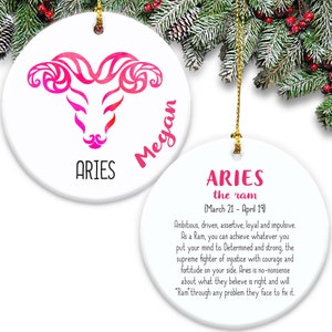 May include: White ceramic Christmas ornament with a pink and red watercolor Aries zodiac symbol and the name Megan. The back of the ornament has the text "ARIES the ram (March 21 - April 19)" and a description of the Aries personality.