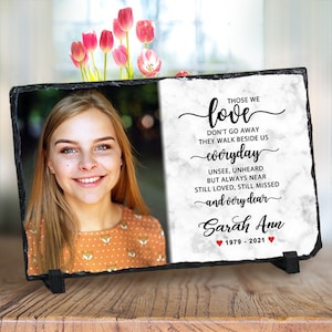May include: A black slate photo memorial with a white marble background. The memorial features a photo of a young woman with a smiling face. The text reads "Those we love don't go away they walk beside us everyday unsee, unheard but always near still loved, still missed and very dear Sarah Ann 1979-2021".