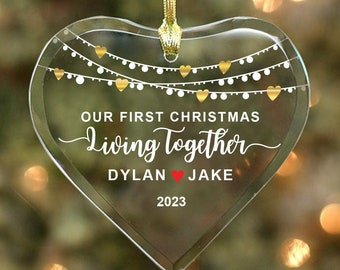 May include: A clear glass heart-shaped Christmas ornament with gold and white string lights and the text "Our First Christmas Living Together Dylan Jake 2023".