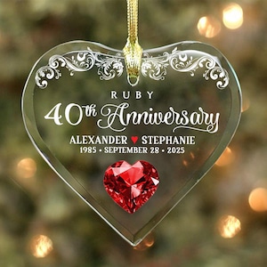 May include: A clear, heart-shaped ornament with the text "RUBY 40th Anniversary" in white script. The ornament features the names "ALEXANDER ❤️ STEPHANIE" and the date "1985 • SEPTEMBER 28 • 2025". A red heart-shaped gem is at the bottom.