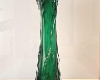 May include: A tall, elegant green glass vase with a unique, organic shape. The vase has a dark green base that transitions to a vibrant, lighter green towards the top. The rim has a textured, ruffled design.