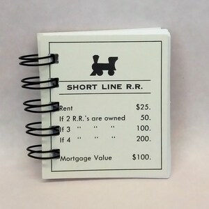 May include: A small spiral-bound notebook with a white cover featuring the text "SHORT LINE R.R." and a train icon. The notebook displays rent and mortgage values in dollars.