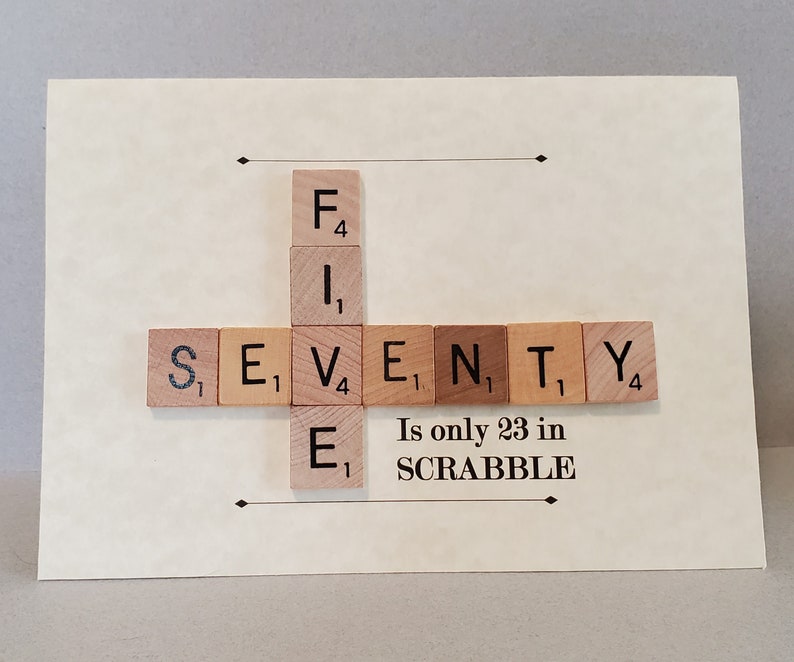May include: A card with the word "SEVENTY" spelled out using Scrabble tiles. The tiles are arranged in a cross shape with the word "F.I.E." spelled vertically. The card also includes the text "Is only 23 in SCRABBLE."