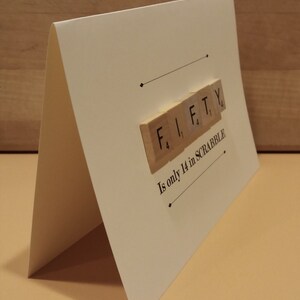 May include: A white card with the word "FIFTY" spelled out in Scrabble tiles. The text below reads "Is only 14 in SCRABBLE".