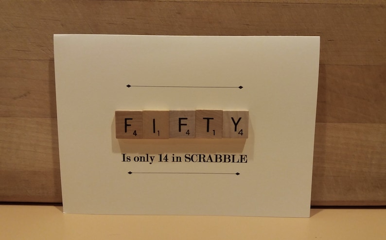 May include: A white card with the word "FIFTY" spelled out using Scrabble tiles. The tiles are arranged in a line and the point values are visible on each tile. The text "Is only 14 in SCRABBLE" is printed below the tiles.