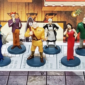 May include: A board game with seven character figurines. The figurines stand on blue bases and represent different characters. The game board is visible with text indicating suspects, weapons, and rooms. The characters are dressed in various outfits.
