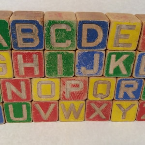 May include: A set of vintage wooden alphabet blocks. Each block is painted in a different colour, including green, blue, yellow, and red. The letters are carved into the wood and painted in a contrasting colour.